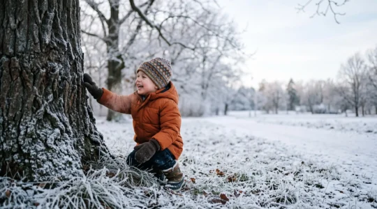 A bundled-up child crouching in a winter park, gently touching the frosty texture of a tree trunk during a sensory scavenger hunt