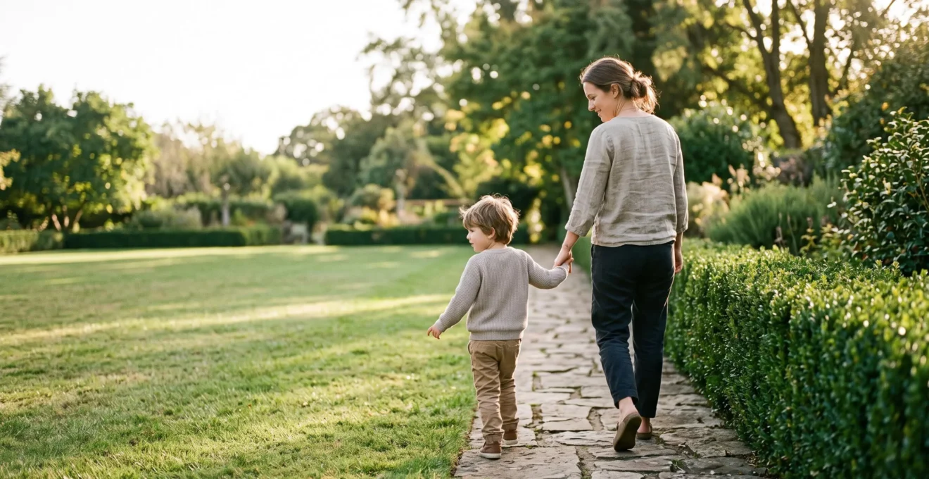 A parent and child walking together along a garden path with a subtle low hedge marking a boundary, symbolizing the line between warmth and limits in parenting